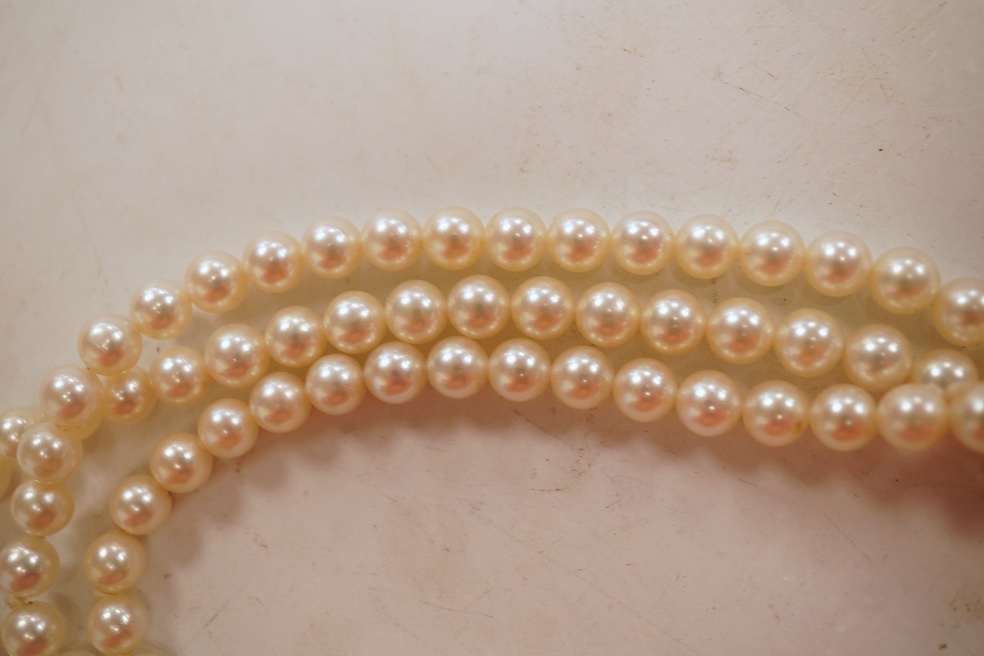 A cultured pearl, ruby and diamond clasp, composed of three rows of cultured pearls measuring approximately 6.9mm diameter, to a white precious metal (tests as 14k) disc-shaped clasp pavé-set with brilliant-cut diamonds